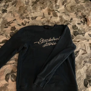 Mörkblå tröja från Stockholm Stories - Säljer en stilren mörkblå tröja från Stockholm Stories med text på bröstet. Tröjan har långa ärmar och en rund halsringning. Perfekt för en avslappnad stil.