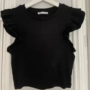 Säljer en svart ribbad topp från Zara med volanger vid ärmarna. Använd en gång så är som ny. Storlek S❣️
