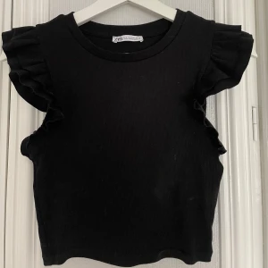 Svart ribbad topp från Zara - Säljer en svart ribbad topp från Zara med volanger vid ärmarna. Använd en gång så är som ny. Storlek S❣️