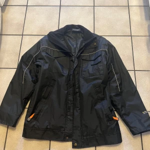 Svart jacka från Bluewear - Säljer en svart jacka från Bluewear med dragkedja och knappar. Jackan har långa ärmar och flera praktiska fickor. Den är perfekt för kyligare väder med sin fodrade insida.