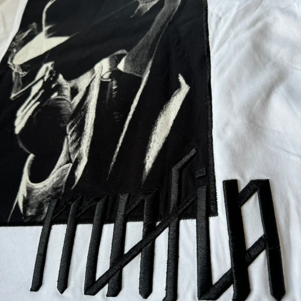 Snygg oversizedvit t-shirt från GANGS med ett stort svart tryck av en person i hatt och texten 'mafia' broderad på baksidan. Perfekt för en cool och avslappnad stil. Perfekt till gymmet också för någon som gillar att träna i oversized t-Shirt. Har fler storlekar i profilen. . T-paidat.