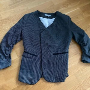 Svartvit kavaj med diskret mönster - Snygg svartvit kavaj med ett diskret rutigt mönster. Kavajen har en elegant passform och är perfekt för en stilren look. Den har 3/4 ärmar och en enkel knäppning framtill.