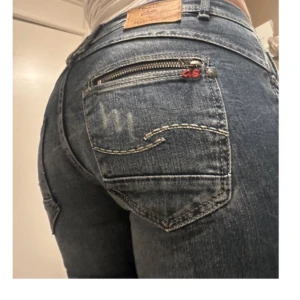 Blå lågmidjade jeans med dragkedja från Q/S designed by denim goods - Snygga blå jeans från Q/S designed by med dragkedja på bakfickan och femficksdesign. Midjan är märkt med 'For you with love' Aldrig använt, då de sitter för tight. Sygg dragkedja på högra bakre fickan. De är i storlek w/34 L/32 men passar mig som vanligtvis har 27/32. De är i usa storlek och är därför mindre. Skriv för frågor 💕