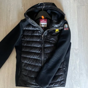 Svart cardigan från Parajumpers - Säljer en svart jacka från Parajumpers med huva och dragkedja. Jackan har quiltade paneler och en broderad logga på ärmen. Cardiganen är i modellen nolan och är i strlk Y-m passar runt 160-170cm👌4k nypris å cardiganen är i mycket bra skick. Tveka inte på att höra av dig om du har frågor eller vill ha fler bilder 🤗detta är intressekoll 