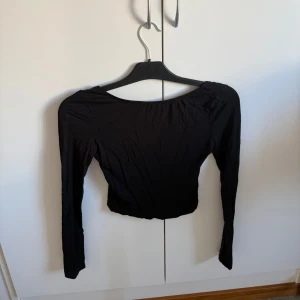 Svart långärmad topp - Snygg svart långärmad topp med en tight passform. Perfekt för en stilren look. Toppen är enkel och elegant, vilket gör den lätt att matcha med olika outfits. med öppen rygg.