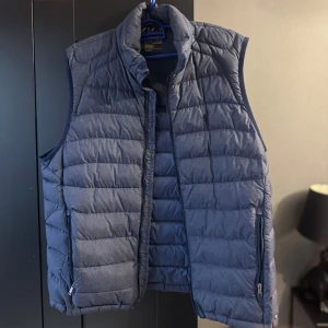 Blå dunväst från Ralph Lauren - Snygg blå dunväst från Polo Ralph Lauren, i storlek M. Säljer för 500kr då man behöver sätta dit ny dragkedja då den har lossnat. 