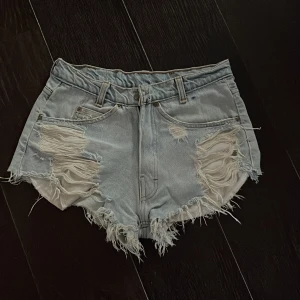 Ljusa jeansshorts från Levi's - Säljer ett par ljusa jeansshorts från Levi's med fransiga kanter och slitna detaljer. Perfekta för en avslappnad stil. De har en klassisk femficksdesign och en läderetikett baktill.