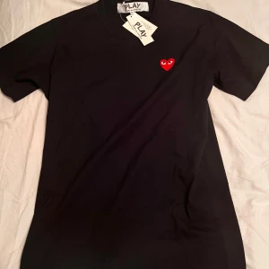 Svart cdg  t-shirt med rött hjärta - Säljer denna feta Comme des Garcons T-shirt för ett bra pris. Den är i storlek M och passar kring 180-185 längden. Perfekt för en avslappnad stil. Skriv vid frågor eller funderingar☺️