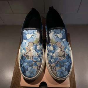 Gucci loafers - Säljer nu dessa feta Gucci GG Supreme canvas slip ons med det unika Blue Blooms flower Print. Skon är av ett tjockare och slittåligt läder. 2600kr öppen för diskution.