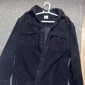 Svart manchester overshirt från H&M - Snygg svart manchester overshirt från H&M med knappar framtill och två bröstfickor. Perfekt för lager-på-lager-stil. Passar bra till både vardag och mer avslappnade tillfällen.