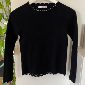 Svart långärmad tröja från MNG! XS - Snygg svart långärmad tröja från MNG Basics med vågig kantdetalj vid hals och nederkant. Perfekt för en stilren look. Tröjan är i en mjuk och bekväm kvalitet. Tröjan har inga skador eller anmärkningar eller noppror! Fint skick. Den har små tunna ribbade linjer. Fin kvalite på tyget! 