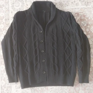 Svart stickad kofta med knappar - Säljer en stilren svart stickad kofta med knappar framtill. Koftan har ett snyggt kabelstickat mönster och långa ärmar. Perfekt för kyligare dagar.