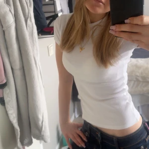 Vit ribbad kortärmad topp - Säljer en stilren vit ribbad topp med korta ärmar. Perfekt för en avslappnad look. Toppen är figurnära och passar bra till jeans eller kjol.