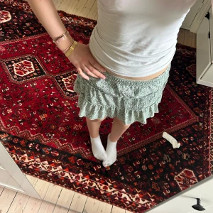Grön blommig volangkjol från Zara - Supersöt grön kjol från Zara med blommönster och  volanger. Kjolen är kort och har en elastisk midja, och är luftig och skön. Perfekt för vår och sommar!☀️❤️storlek 164, skulle säga att den är xs-s. Tveka inte att kontakta vid frågor eller funderingar ❤️de är inbyggda shorts vilket ger en trygghet!
