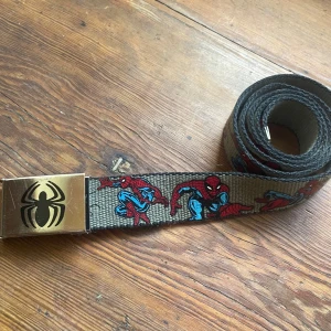 Spiderman bälte ( Marvel ) - Säljer ett fett bälte med Spiderman-motiv och metallspänne med svart spindel-logga. Bältet är grått med Spiderman som gör olika poser. Bara att fråga efter mått & andra funderingar. 