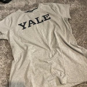 Grå t-shirt  - Grå t-shirt med marinblått Yale tryck över bröstet. T-shirten har rund halsringning och är kortärmad. 