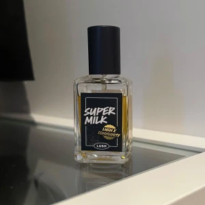 Super Milk parfym från Lush - Super Milk parfym från Lush i en genomskinlig, fyrkantig glasflaska med svart etikett och svart lock. Parfymen har en gulaktig vätska och modern design. Perfekt för dig som gillar unika dofter och snygga flaskor. 