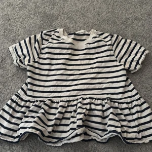 Randig tröja från Zara - Supersöt tröja från Zara i vitt med marinblå/svarta ränder. Tröjan har korta ärmar, rund halsringning och volang nedtill. Perfekt för en varm sommarkväll!! Har någon liten fläck här och där men jag skulle inte säga att det märks tydligt när man har på sig den.😊🌸💕