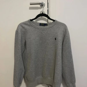 Grå sweatshirt från Polo Ralph Lauren - Klassisk grå sweatshirt från Polo Ralph Lauren med rund halsringning och broderad svart logga på bröstet. Skriv vid intresse 