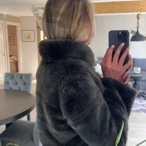 Mörkbrun pälsjacka - Säljer en snygg mörkbrun/grå  pälsjacka med krage. Jackan har lång ärm och en klassisk, lyxig look. Perfekt för att höja stilen under kallare dagar. Passar dig som gillar trendiga och tidlösa plagg. Enda defekten är att det börjar släppa inuti matrial vid lappen där märket står