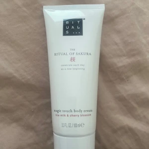 The Ritual of Sakura Magic Touch Body Cream - En lyxig body cream från Rituals, The Ritual of Sakura, med doft av ris-mjölk och körsbärsblom. Kommer i en vit tub på 100 ml, perfekt för att återfukta huden och ge en fräsch känsla.