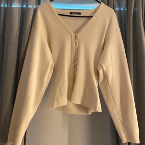  kofta med knappar från Gina Tricot - Säljer en beige/krämfärgad kofta från Gina Tricot i storlek XS. Koftan har v-ringning, långa ärmar och knappar framtill. Materialet är mjukt och känns som stickad bomull. Perfekt att slänga över en topp för en enkel och stilren look. Finns en liten prick på vänstra armen som jag inte kan få bort