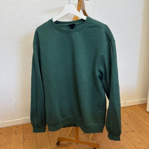 Grön sweatshirt från H&M - Säljer en grön sweatshirt från H&M i relaxed fit. Tröjan har rund halsringning, långa ärmar och ribbade muddar vid ärmslut och nederkant. Perfekt för en avslappnad stil.