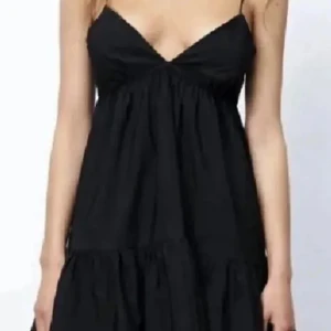 Svart kort klänning med smala axelband - Säljer en svart kort klänning med smala axelband och v-ringning. Klänningen har en luftig passform och volang nedtill, perfekt för varma dagar. Enkel och stilren design som passar till många tillfällen.