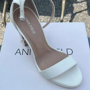 Vita sandaler med klack från Anna Field - Säljer ett par stilrena vita sandaler från Anna Field med öppen tå och klack. Skorna har en enkel rem över tårna och en justerbar rem runt vristen. Perfekta för vår och sommar! Storlek 38