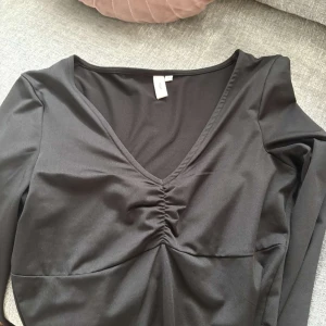 Svart långärmad topp med v-ringning från Nelly - Säljer en svart långärmad topp från Nelly med snygg v-ringning och rynkdetalj framtill. 