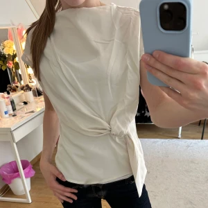 Vit omlottopp med knytdetalj - Säljer en stilren vit omlottopp med knytdetalj i midjan. Toppen har korta ärmar och en elegant, något lös passform. Perfekt att styla till både jeans och kjol för en fräsch look.💕Tröjan är i xxs men skulle säga att den passar också xs och s.