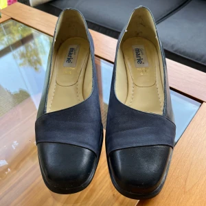 Mörkblå  pumps från Marie - Klassisk mörkblå pumps från Marie med låg klack och rund tå. Skorna har en matt finish med en diskret glansig detalj framtilll.. Storlek 39. Endast använda ett par gånger. 