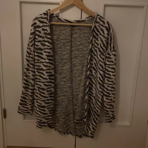 Zebramönstrad cardigan med glitterdetaljer - Säljer en långärmad cardigan med zebramönster i svart och vitt samt inslag av glittriga trådar. Jackan är öppen framtill och har en avslappnad passform. Perfekt för dig som vill sticka ut lite extra.
