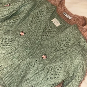 Grön stickad kofta med blommiga knappar från Zara - Superfin ljusgrön stickad kofta från Zara med dekorativa blommiga knappar och hålmönster. Koftan har v-ringning och långa ärmar, perfekt för lager-på-lager-stil.