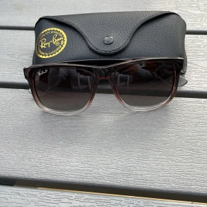 Ray-Ban solglasögon med svart fodral - Snygga Ray-Ban solglasögon med fyrkantig form och mörktonade glas. Bågarna är bruna med transparent nedre del och har Ray-Ban-logga på sidan. Kommer med svart fodral och putsduk.