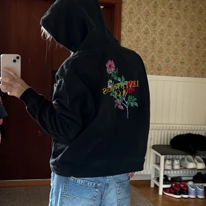 Svart hoodie från Levi's med blommigt broderi - Säljer min svarta hoodie stl xs från Levi's då det inte är min stil längre, den har broderad blomma och text på ryggen. Streetwear och jätte skön, bara inte min stil längre. Sitter oversized. Stor ficka i fram och stor skön luva. 