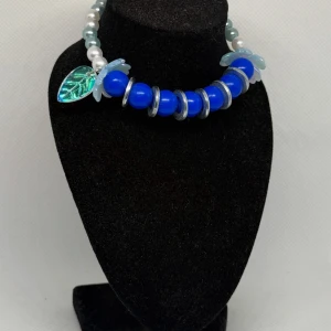 Armband blommor blå sommar - ✨ ”Blue Harmony” – ett kraftfullt blickfång! ✨ Detta handgjorda armband kombinerar djupblå pärlor med skimrande silverfärgade ringar och mjuka blomdetaljer i opalvitt. En glansig grön lövberlock ger smycket en naturnära touch och för tankarna till både hav och skog.  🔹 Färgtoner: Kungsblå, silver, vitt och ljusblått  🔹 Längd: Ca 18–19 cm (elastisk passform) 🔹 Passar perfekt både till vardags och fest   💙 Varje armband är unikt och tillverkat med omsorg – inget är det andra likt!
