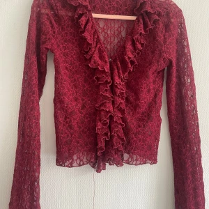 Vinröd spetsblus med volang från Noisy May - Säljer en vinröd, transparent spetsblus (kofta) från Noisy May med långa ärmar och volang längs den djupa v-ringningen. Perfekt för dig som vill sticka ut med en romantisk och trendig look.