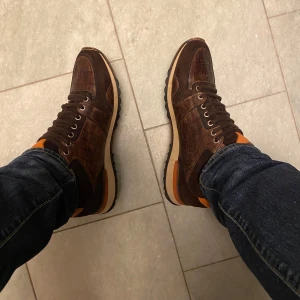 Bruna sneakers med krokodilskinn  - Säljer ett par skor från magnanni.. Skorna har snörning, rund tå och platt sula. Perfekta för dig som vill sticka ut med en unik stil. Krokodilskinn. Nypris:4200kr nyskick. 