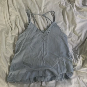 Ljusblå linnetopp med tunna axelband från H&M - Säljer en ljusblå linnetopp från H&M med tunna dubbla axelband och v-ringning. Toppen är ärmlös och har en lätt och luftig känsla, perfekt för varma dagar.