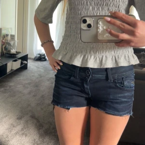 Mörkblå jeansshorts med rå kant - Snygga mörkblå jeansshorts med rå, fransad kant och klassiska fickor fram och bak. Shortsen har låg midja och en slim passform som sitter tajt. Perfekta för varma dagar och enkel att matcha med olika toppar.