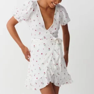 Vit blommig omlottklänning med volang - Superfin vit omlottklänning med puffärmar och volangkant. Djup v-ringning och knyt i midjan ger en feminin look. Perfekt för sommarens alla tillfällen!
