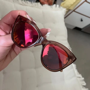 Trendiga solglasögon från Le Specs - Säljer ett par snygga cat eye-solglasögon från Le Specs. De har brun transparent båge och metalliskt röda spegelglas. Märkesdetalj på skalmen. Nyskick!! Använda EN gång. 😎