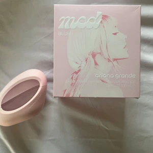 Mod Blush Eau de Parfum av Ariana Grande - En modern parfym från Ariana Grande, Mod Blush, i en unik ljusrosa oval flaska med transparent detalj. Doften kommer i en snygg rosa förpackning med porträtt och präglad text. Perfekt för dig som gillar trendiga och feminina dofter. Flaskan är öppnad men det finns över 70 ml kvar🫶🏻 