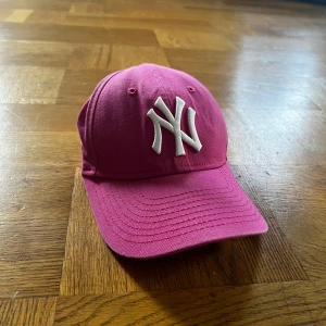 Rosa New York Yankees keps från New Era - Säljer en rosa keps från New Era med New York Yankees-logga broderad i vitt framtill. Modellen är 9FORTY med böjd skärm och justerbar rem baktill. Perfekt accessoar för att lyfta din stil.