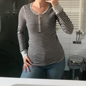 Randig långärmad tröja med knappar - Säljer en svart och vit randig långärmad tröja med rund halsringning och knappdetaljer framtill. Mer som storlek s.