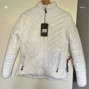 Vit dunjacka från True North - Snygg vit dunjacka från True North med quiltat mönster och hög krage. Jackan har dragkedja framtill och två praktiska fickor med dragkedja. Perfekt för kyliga dagar och enkel att matcha med olika outfits.