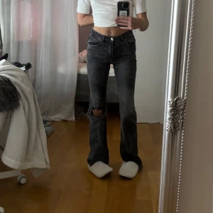 Svarta bootcut jeans med slitningar - Säljer ett par svarta bootcut jeans med snygga slitningar vid knäet och fransiga benslut, dom är lite högre i midjan, långa ben och går till marken på mig som är 170 mc lång