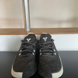 Svarta Nike Kobe sneakers strl 35.5 - Säljer ett par svarta Nike Kobe sneakers med coolt mönstrad mesh och vita detaljer på hälen. Skorna har snörning och rund tå, samt Kobes logga på plös och häl. Perfekta för dig som gillar basketstil och vill sticka ut med en sportig look. Har bara använts inomhus 
