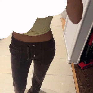 Bruna velourbyxor Juicy Couture XXS - Bruna mjukisbyxor från Juicy Couture i velour med snörning i midjan och stora fickor framtill. Byxorna har en relaxed passform och klassisk Juicy-stil, perfekta för en chill och trendig look.